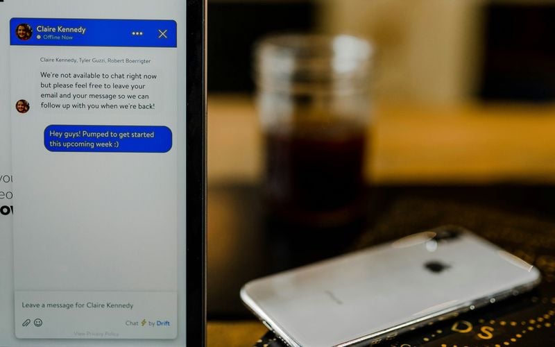 Angeschnittenes Laptop mit Chatbot daneben liegt ein Smartphone auf dem Tisch