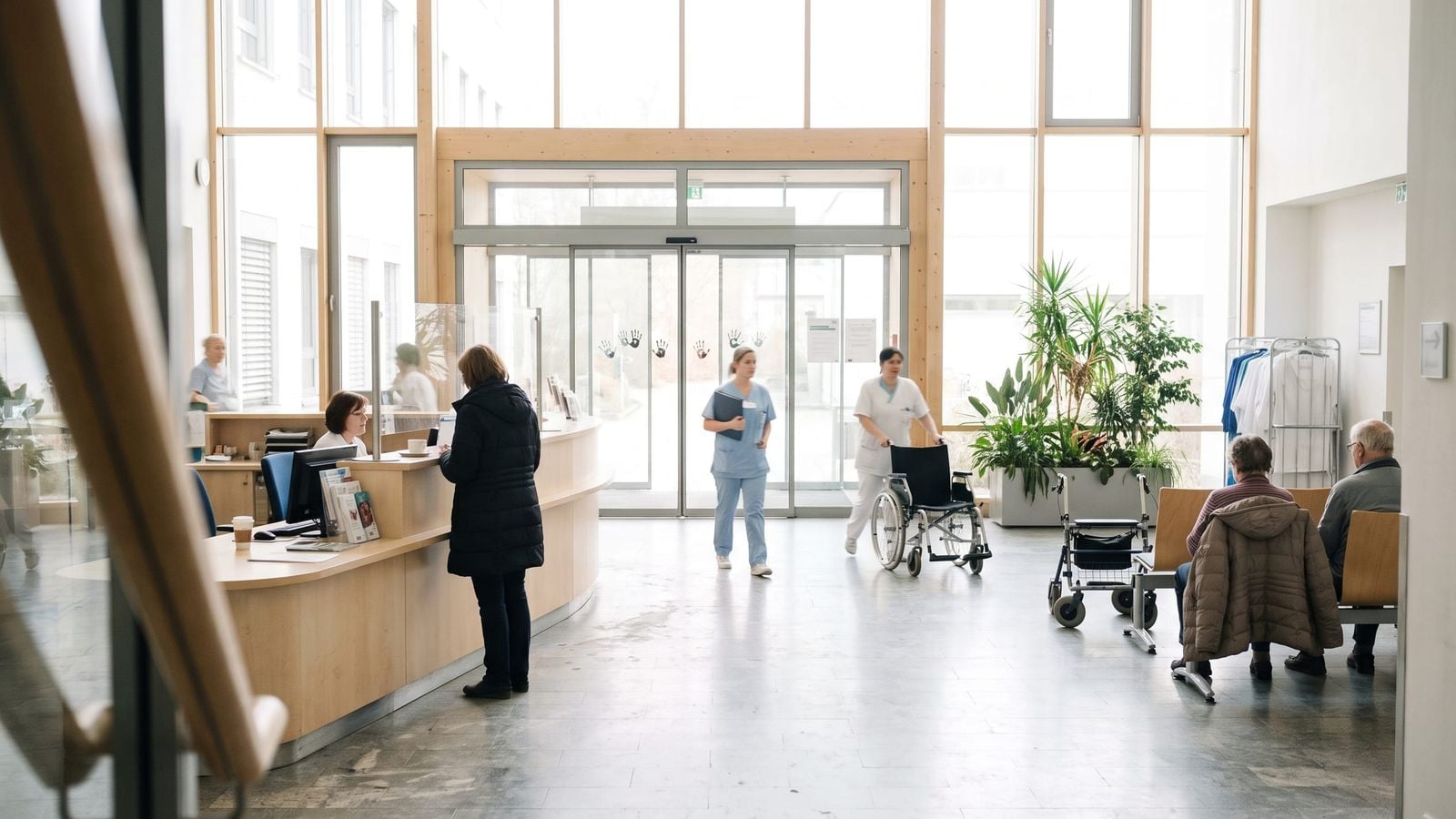 Die helle Eingangshalle eines Krankenhauses mit Empfangstresen, Wartestühlen und Pflegekräften auf dem Weg durch die Halle